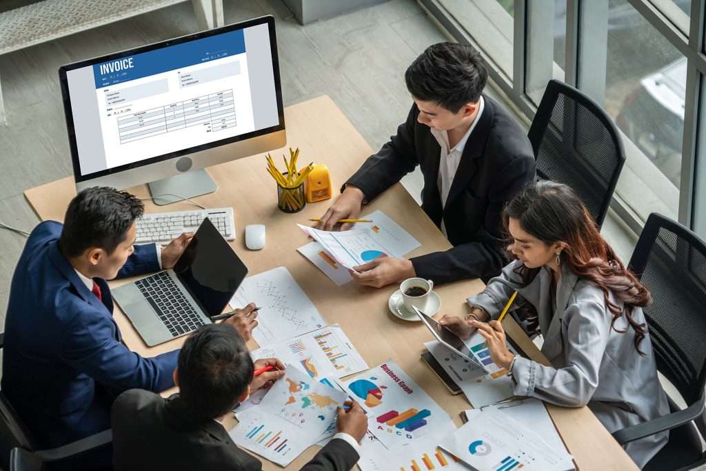 Four colleagues reviewing reports and data on a laptop during a meeting
